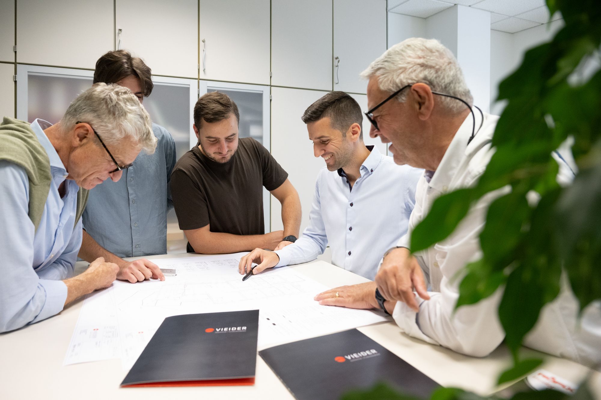 Fünf Männer besprechen gemeinsam an einem Tisch Pläne und Unterlagen in einem Büro.