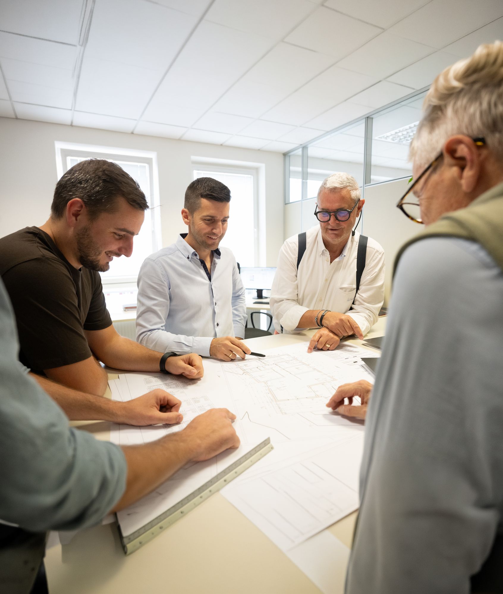Vier Männer besprechen in einem hellen Büro gemeinsam Baupläne an einem Tisch.